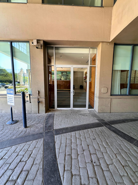 Ground-level view of double glass doors leading into Pier 5’s lobby, with “Visitors” sign and cobblestone pathway in foreground.