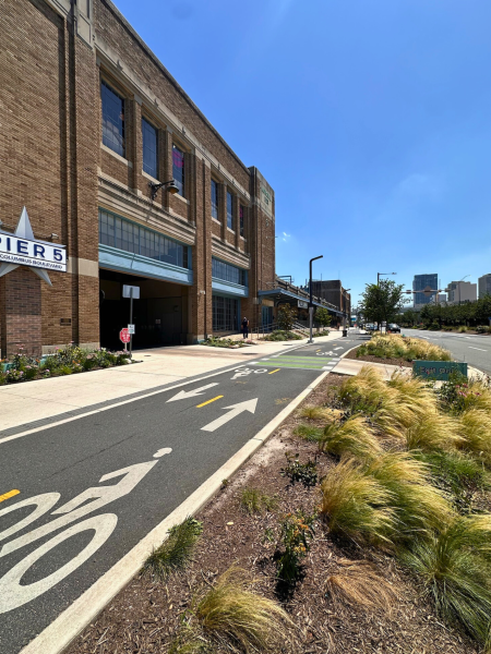 South-facing view of Pier 5 building with protected bike lane and directional arrows, star-shaped “Pier 5” sign, and landscaped median along Columbus Boulevard.
